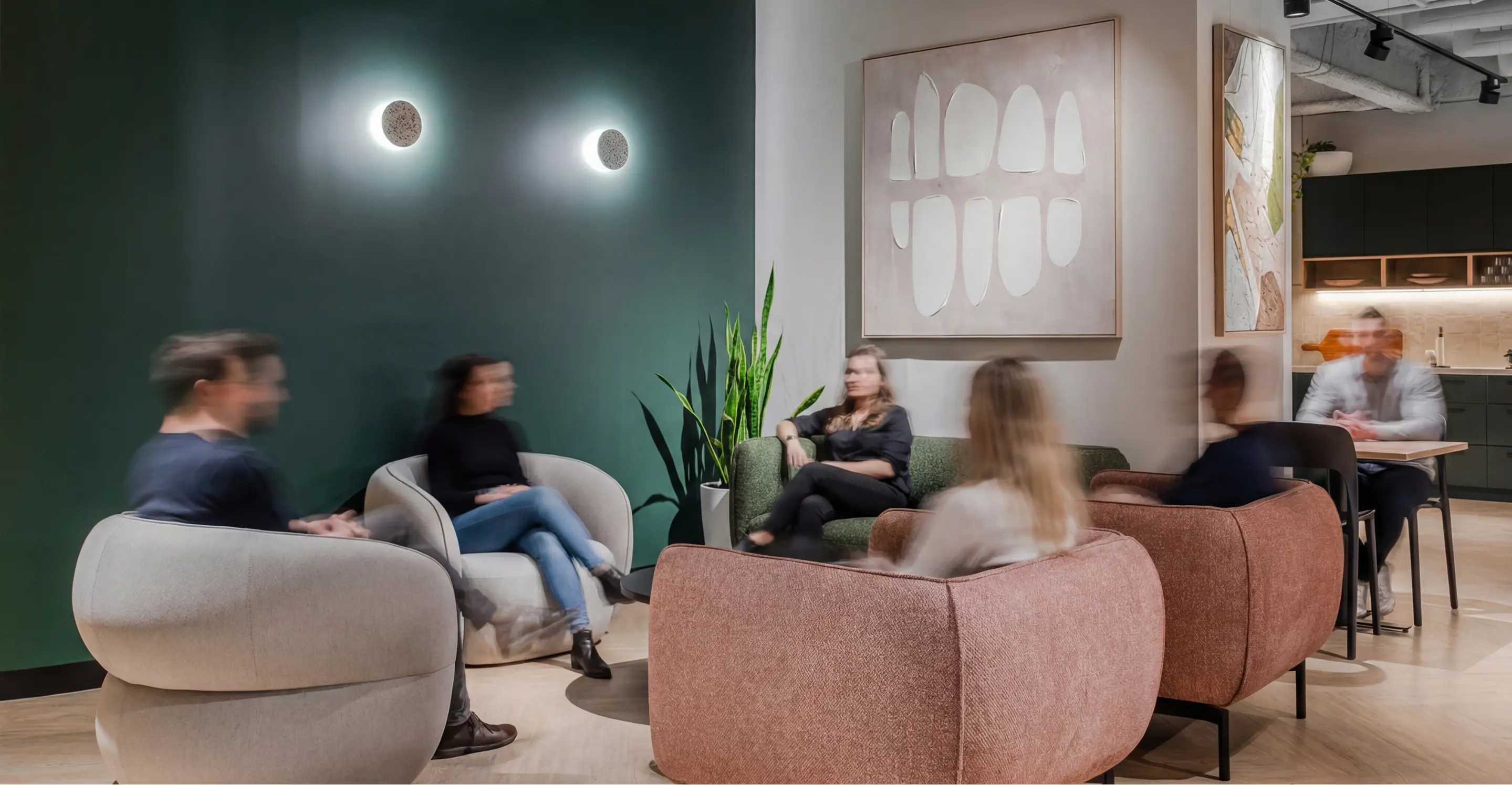 Blurry people sitting in modern armchairs and sofa in a stylish office lounge with green wall and abstract paintings.