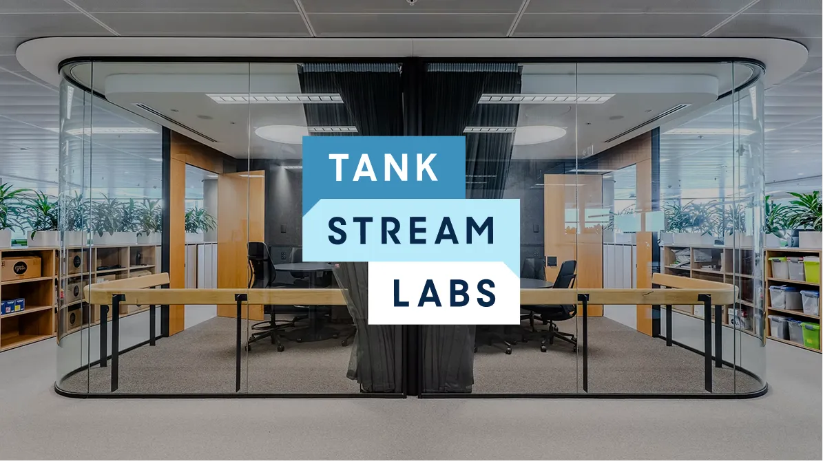 Modern office space with glass-walled conference room and the text TANK STREAM LABS overlaid.