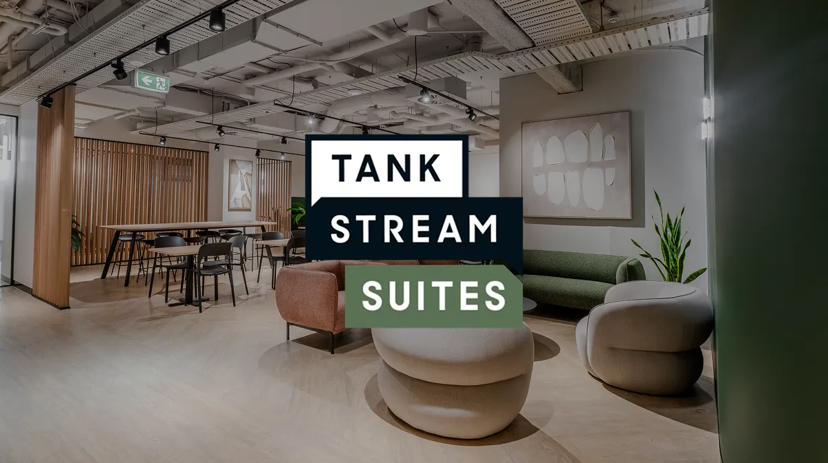 Modern lounge area with stylish armchairs, a green sofa, wooden tables, chairs, and abstract wall art in an open office space.