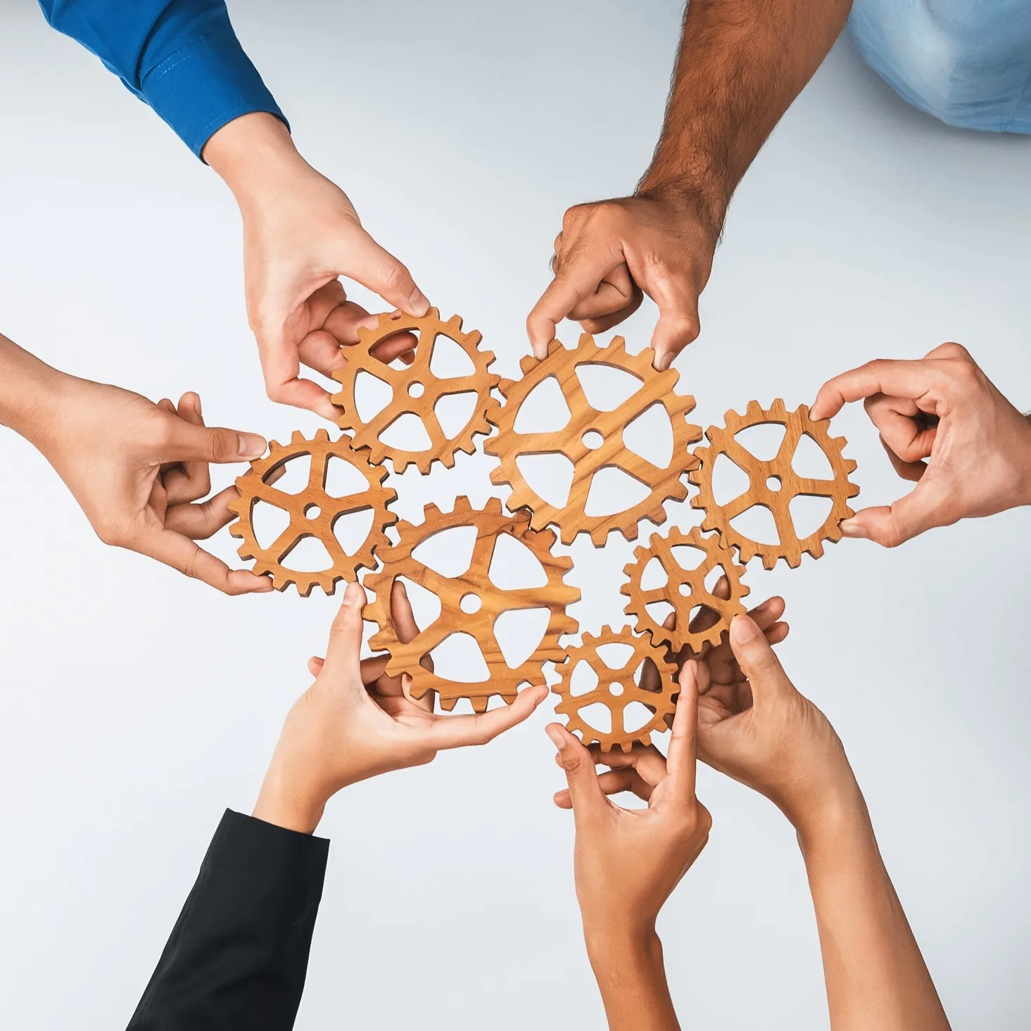 Multiple hands holding and connecting wooden gears symbolizing teamwork and collaboration.