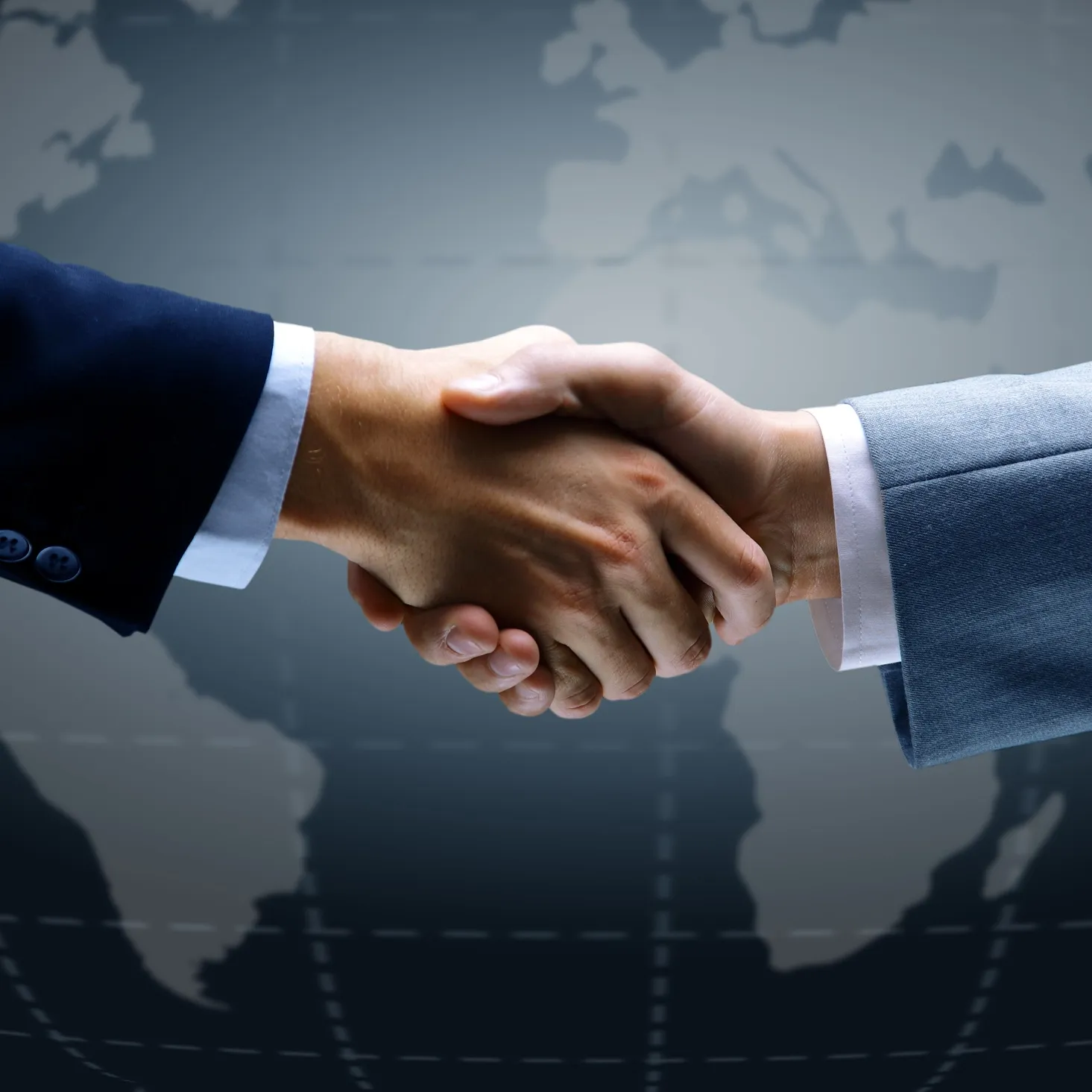 Two people in business suits shaking hands with a blurred world map background.