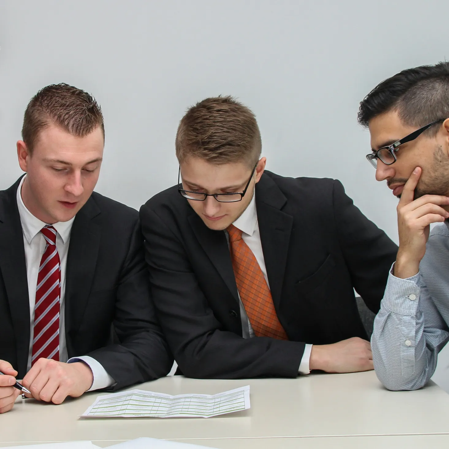 Three men in business attire sitting at a table, reviewing a document together.