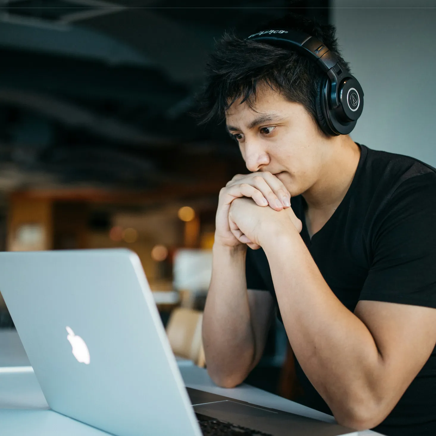 Man wearing headphones intently looking at a laptop screen in a modern indoor setting.