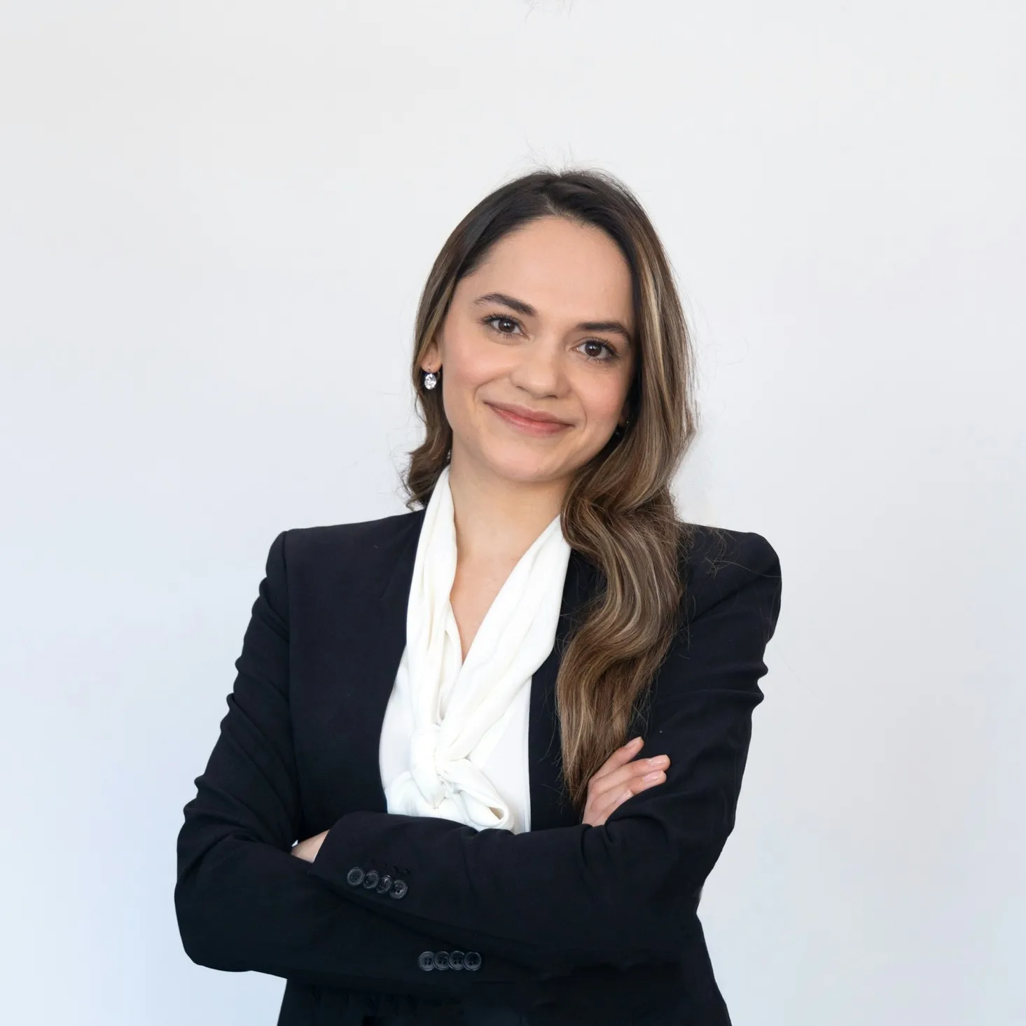 Smiling professional woman with long hair wearing a black blazer and white scarf with arms crossed.
