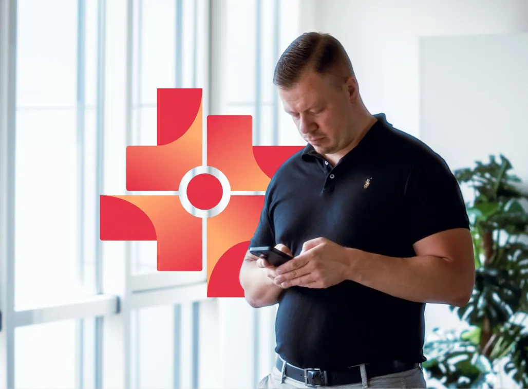Man in black polo shirt looking at his smartphone indoors near plants and large window.