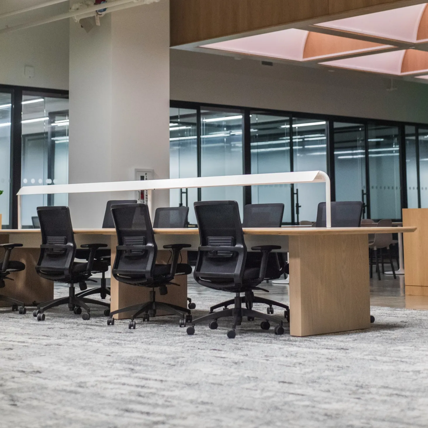 Modern office conference room with black swivel chairs around a large wooden table and glass walls in the background.