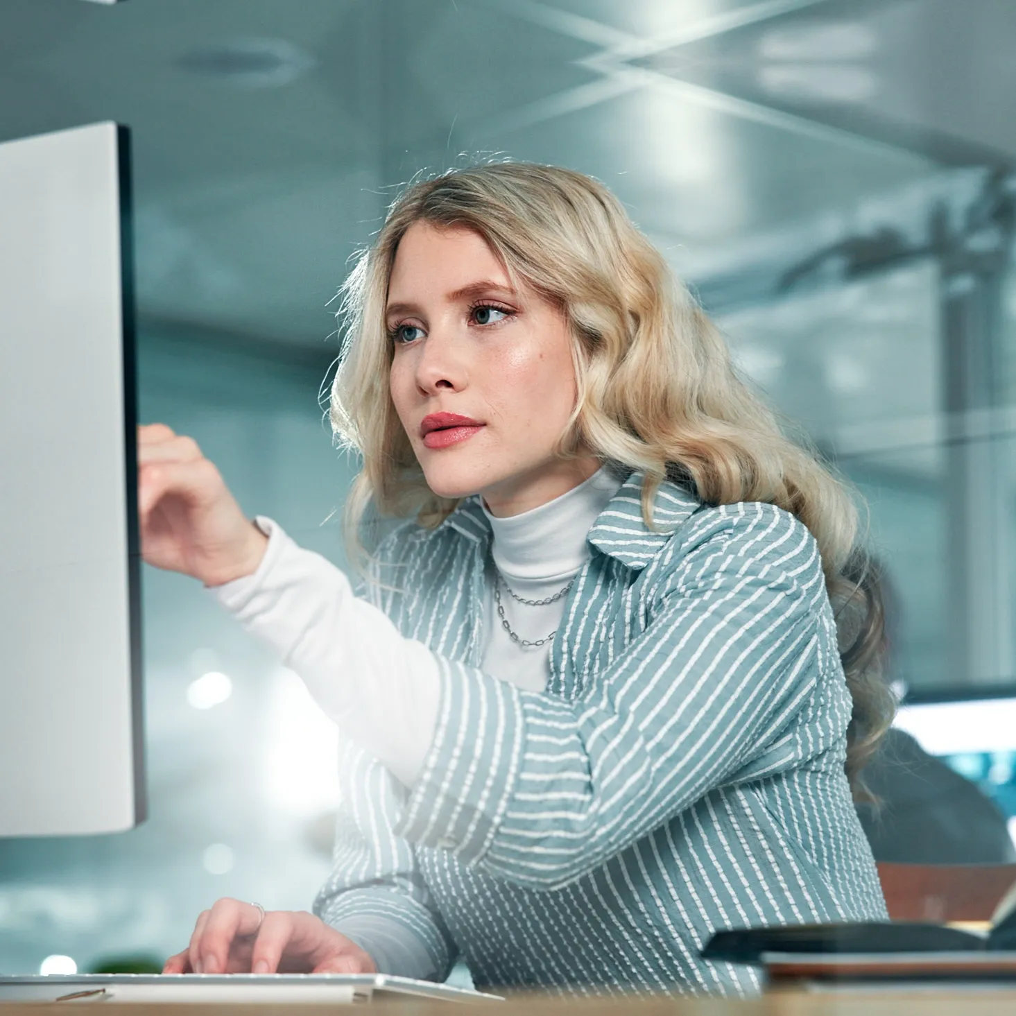 Focused woman with blonde hair working on a computer in a modern office.