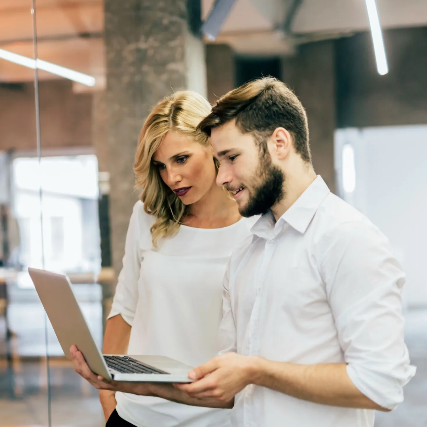 Two colleagues standing close together looking at a laptop screen in a modern office.