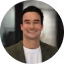 Portret van een lachende man in een donkere coltrui met een geblurde achtergrond.