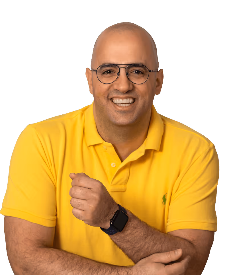 Smiling bald man wearing round glasses and a yellow polo shirt with crossed arms and a smartwatch on his wrist.