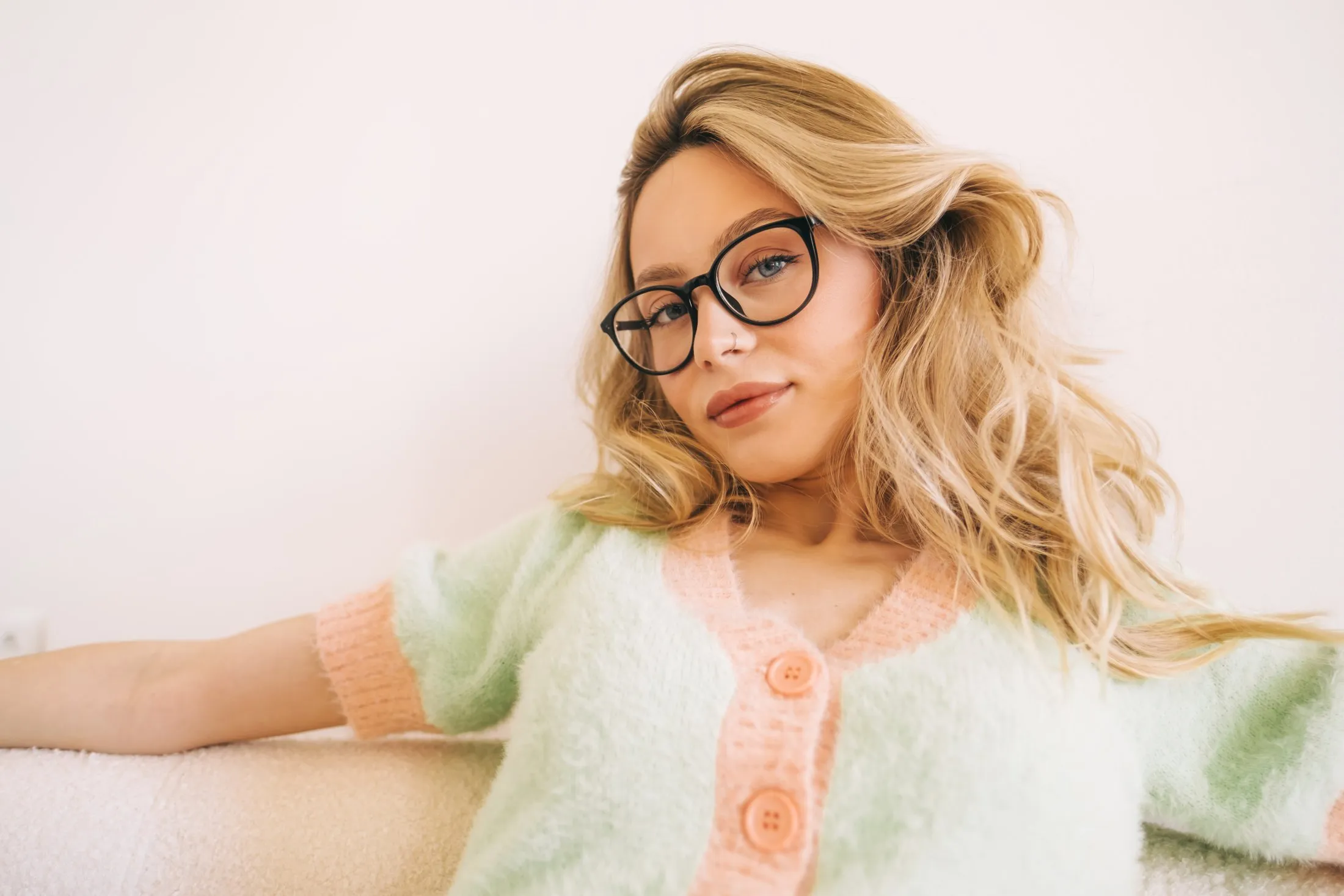 Woman wearing black glasses and pastel cardigan with blonde wavy hair