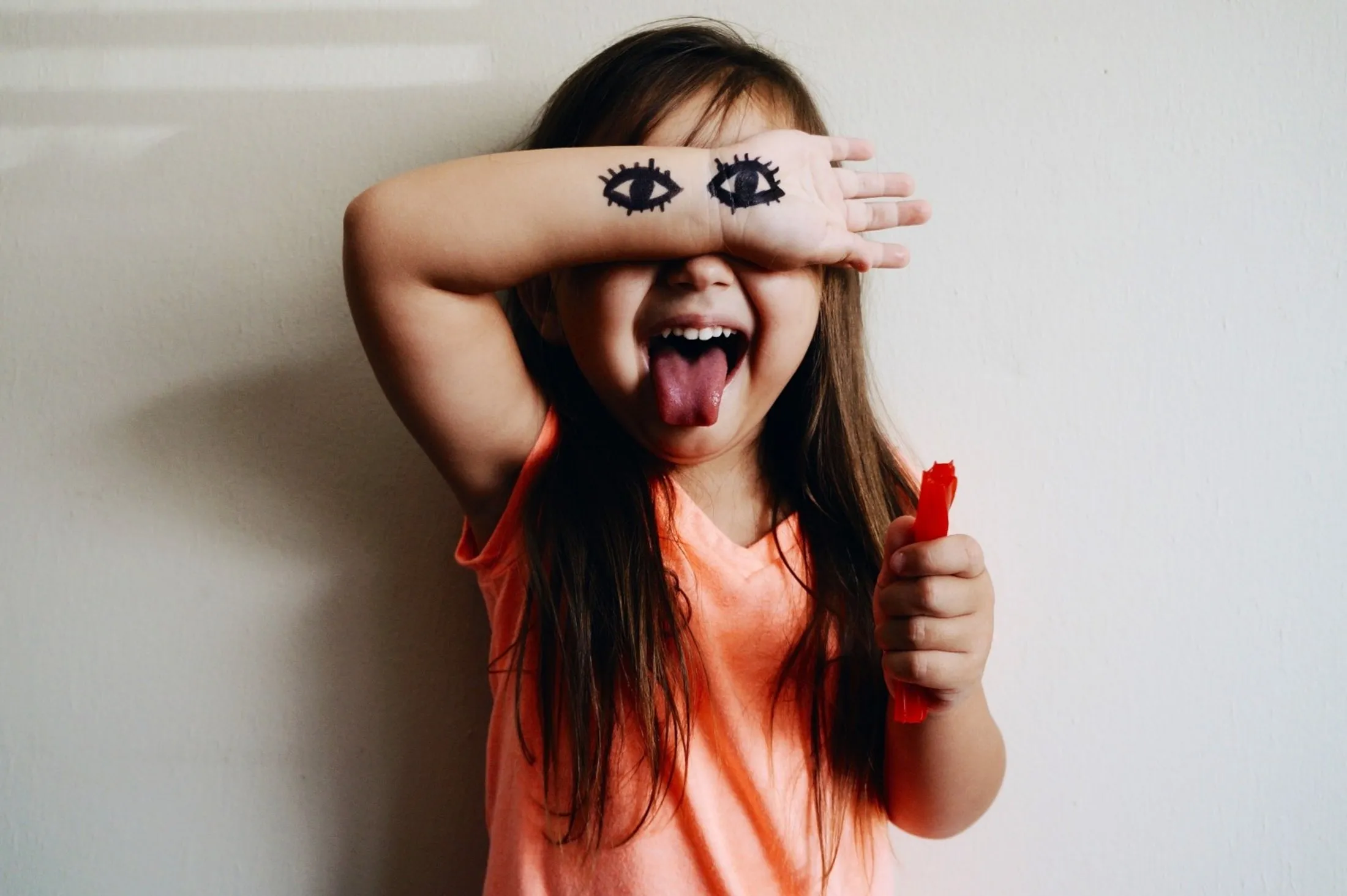 Child in orange shirt with drawn eyes on arm sticking tongue out playfully