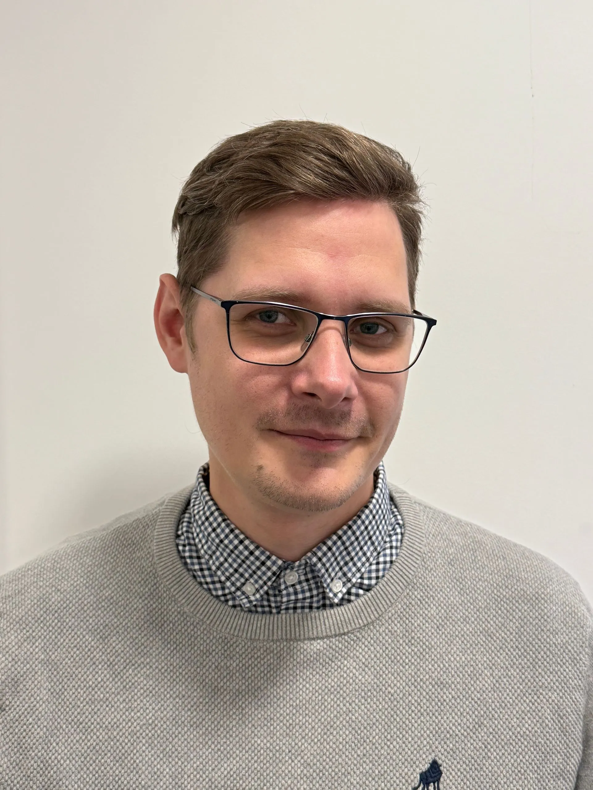 Man wearing glasses and checkered shirt, neutral background, professional headshot portrait.