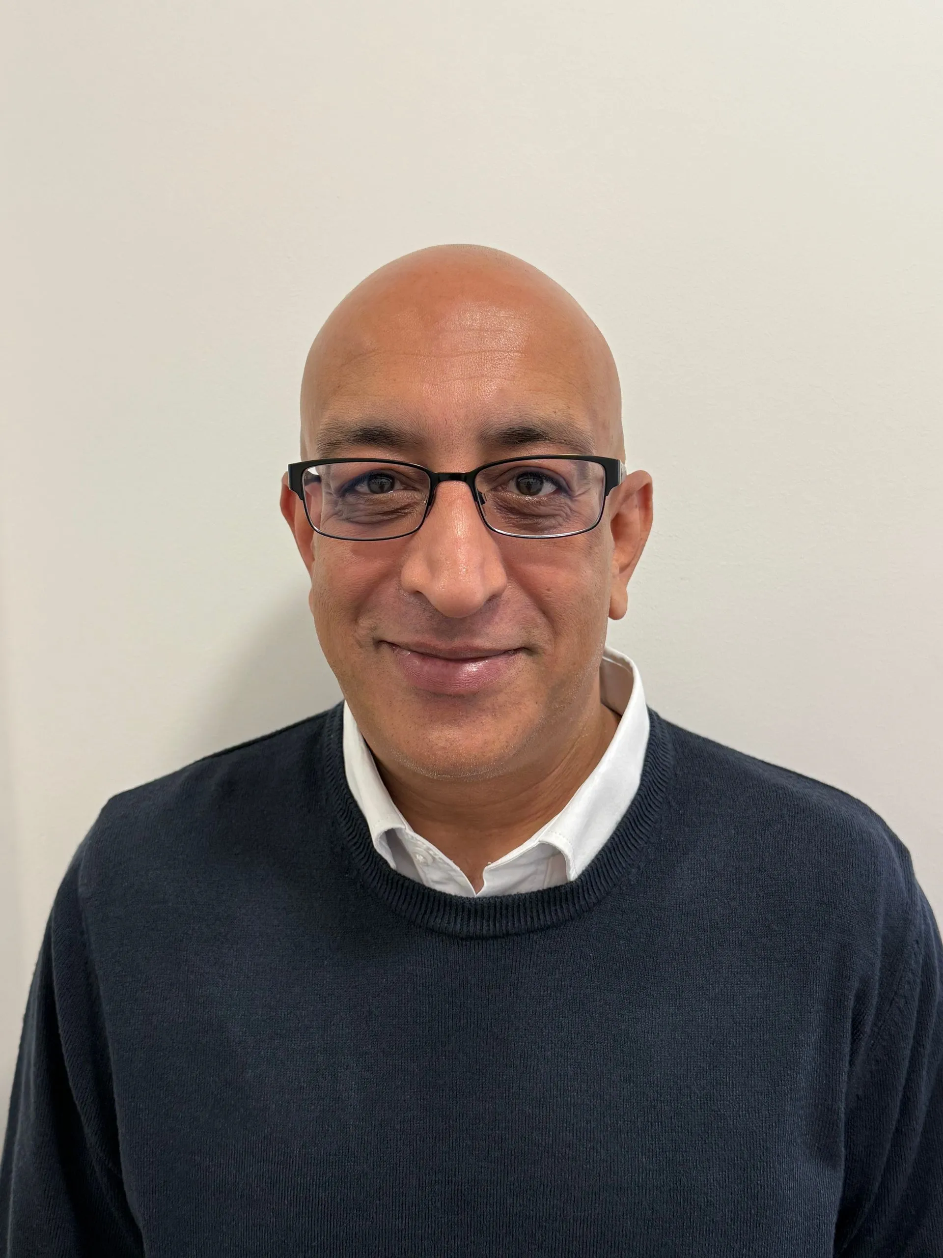 Middle-aged man with glasses wearing dark sweater smiling at camera