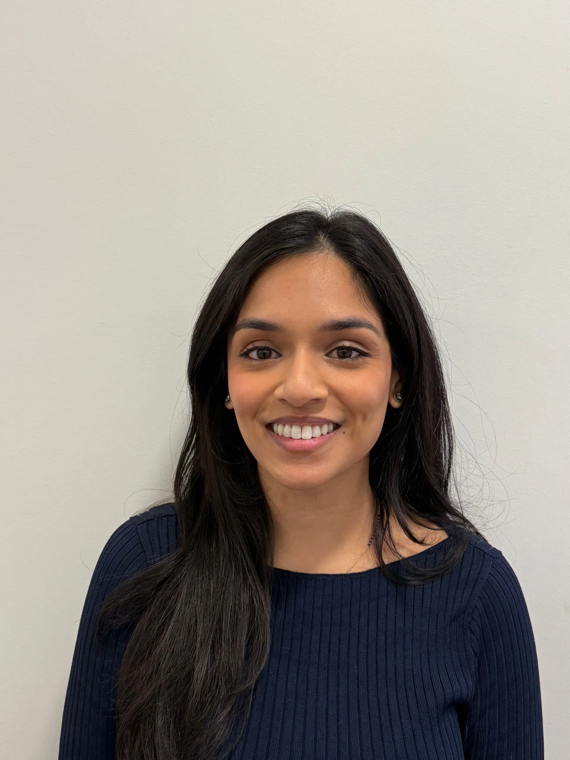Portrait of a smiling woman with long black hair wearing a navy ribbed sweater