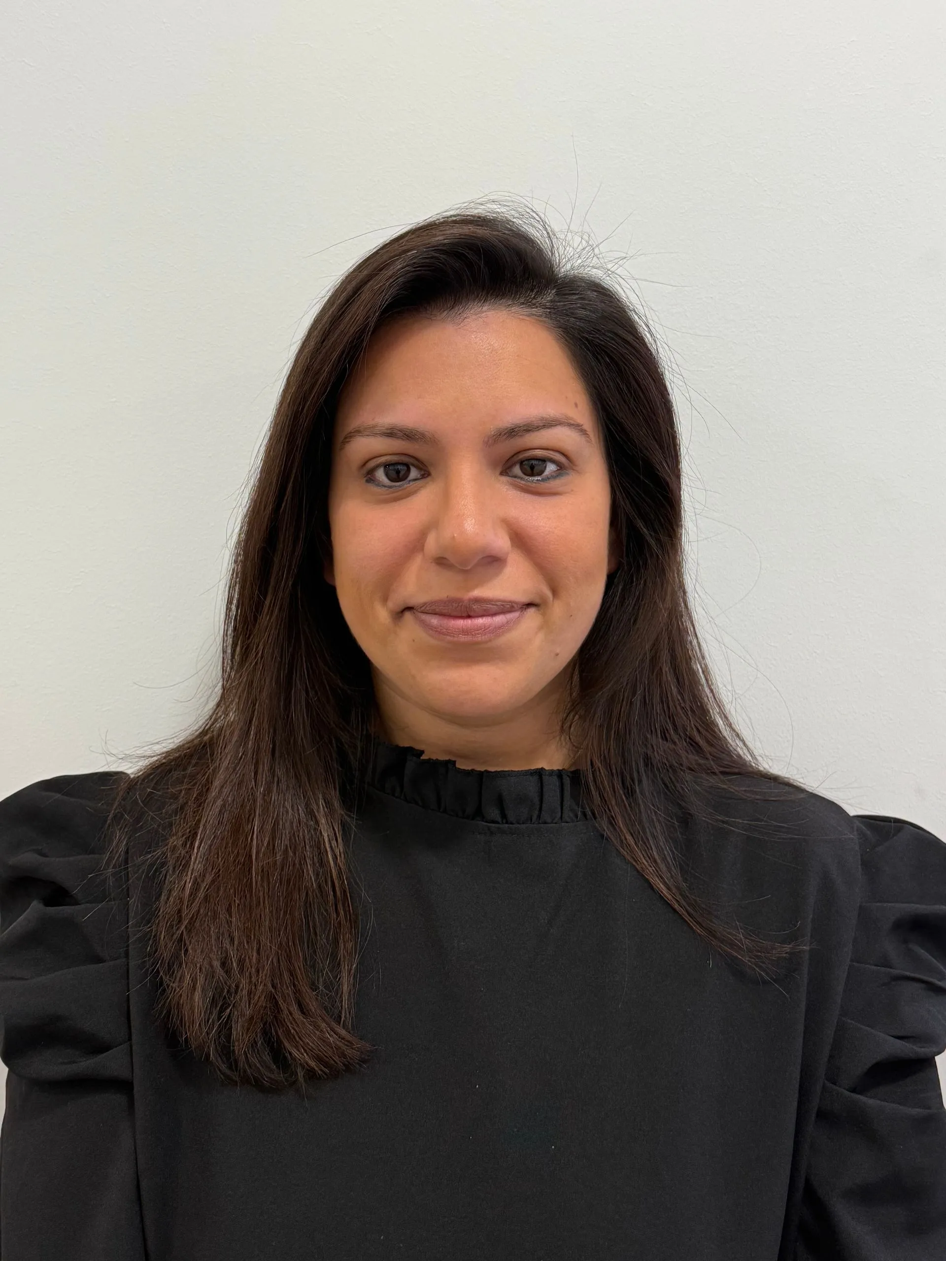 Portrait of woman with long dark hair wearing black turtleneck against plain background