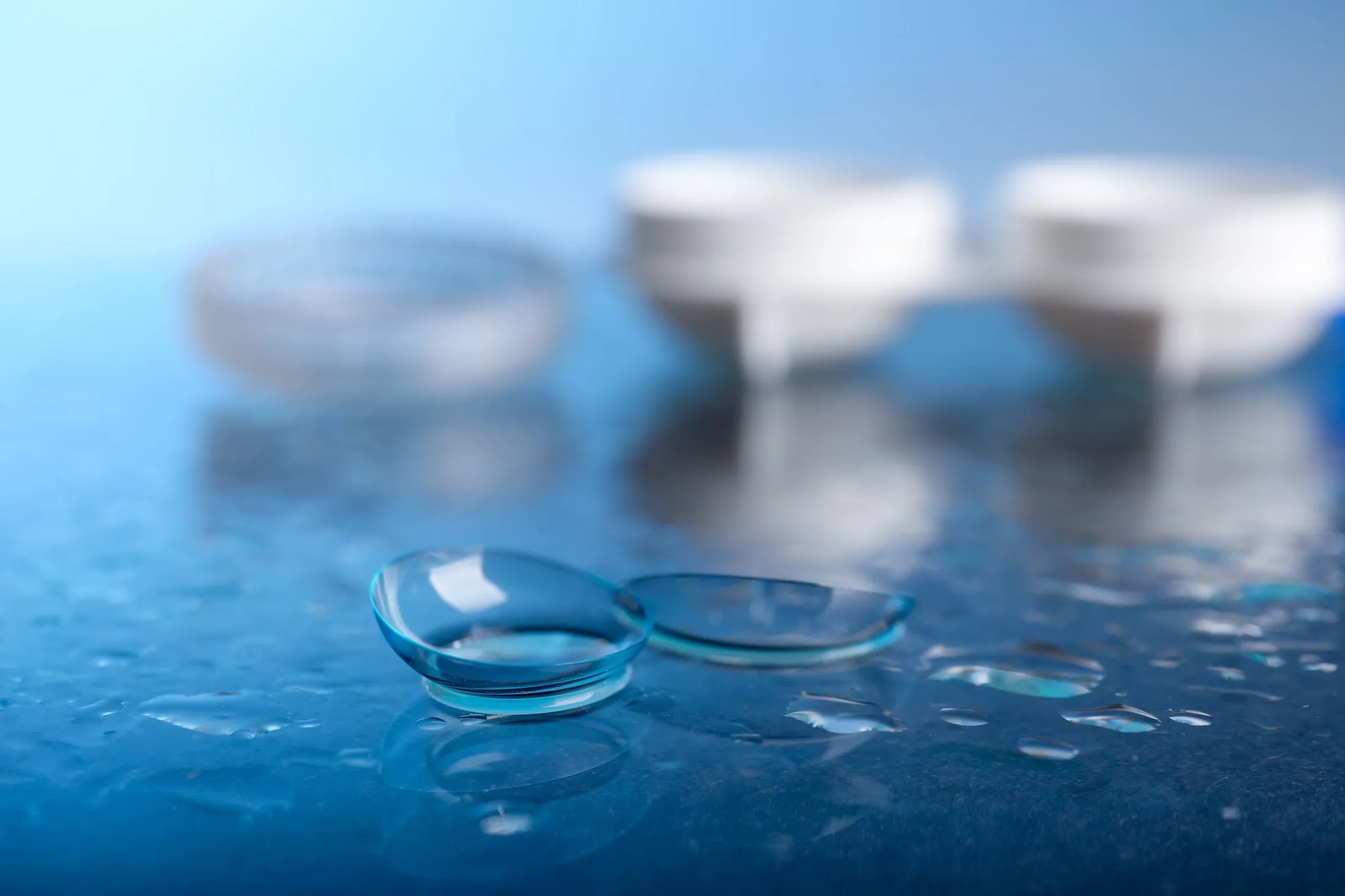 Two blue contact lenses with water droplets on blurred background