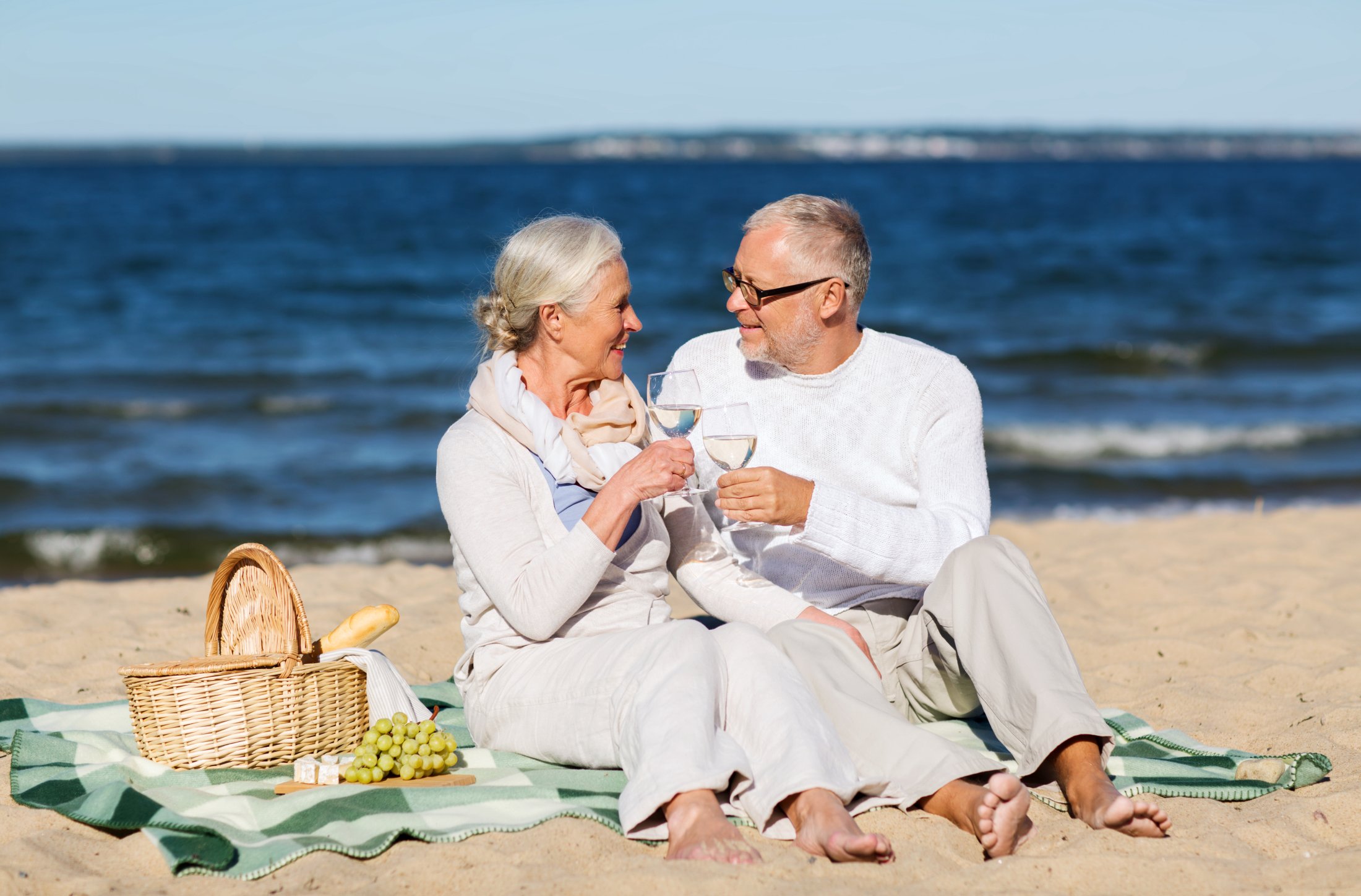 Elderly couple toasts with wine glasses during a beach picnic by the ocean