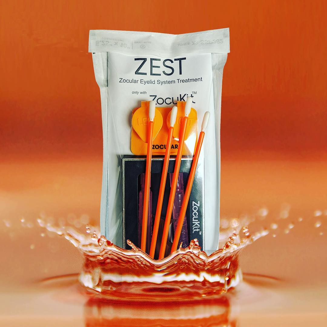 ZEST Zocular Eyelid System Treatment kit with orange applicators and orange liquid splash background.
