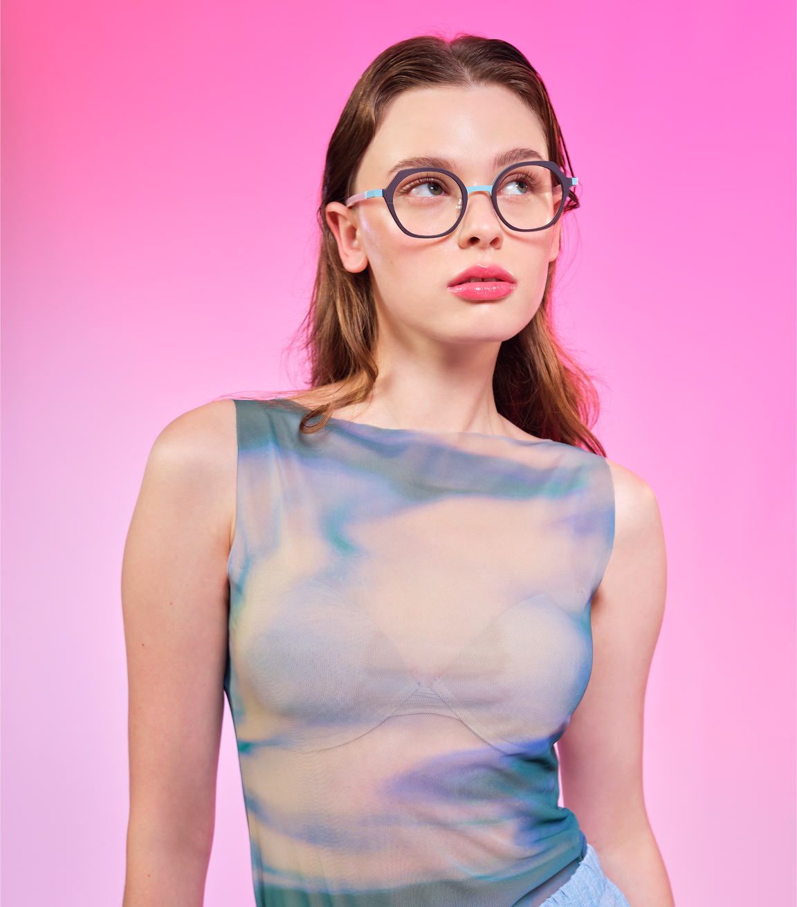 Woman with glasses wearing tie-dye top against bright pink background