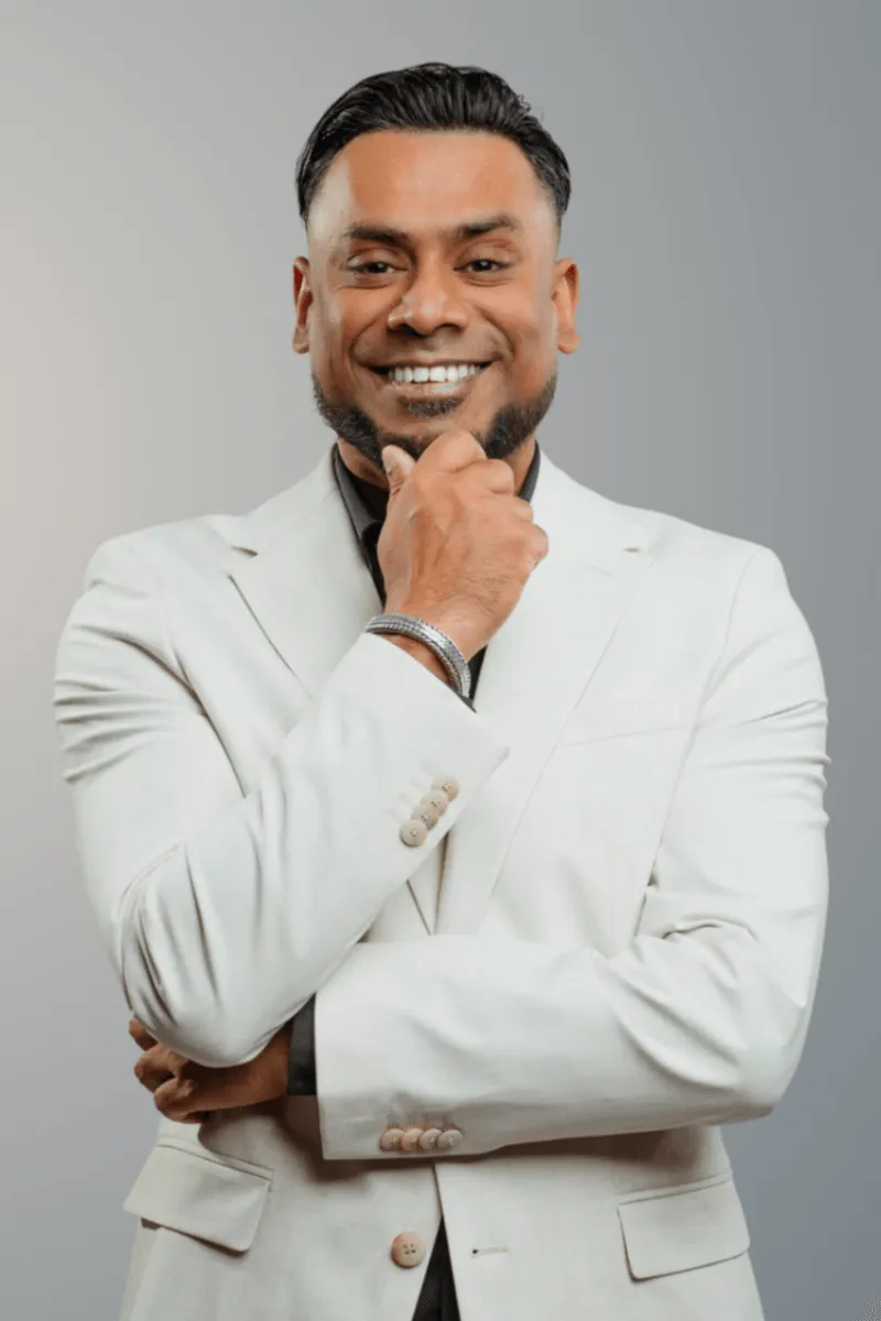 Man met een beige pak die glimlacht met zijn hand tegen zijn kin.