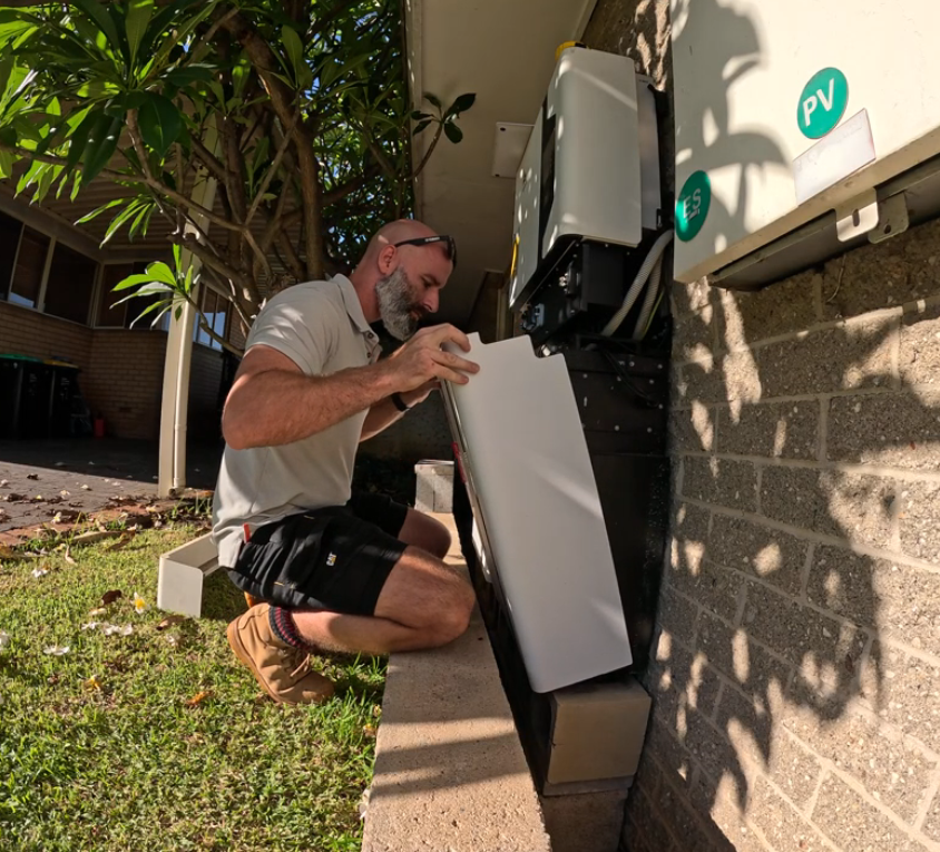 Electrician with a beard installing or repairing a wall electrical outlet using a screwdriver.