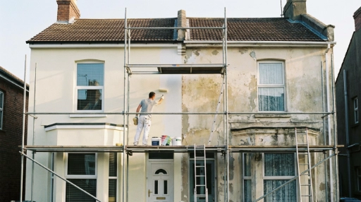 Ein Maler trägt Gerüst bei der Renovierung und dem Anstrich der Fassade eines zweistöckigen Hauses.