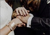 Bride and groom holding hands during a wedding ceremony, showing wedding bands and detailed attire.