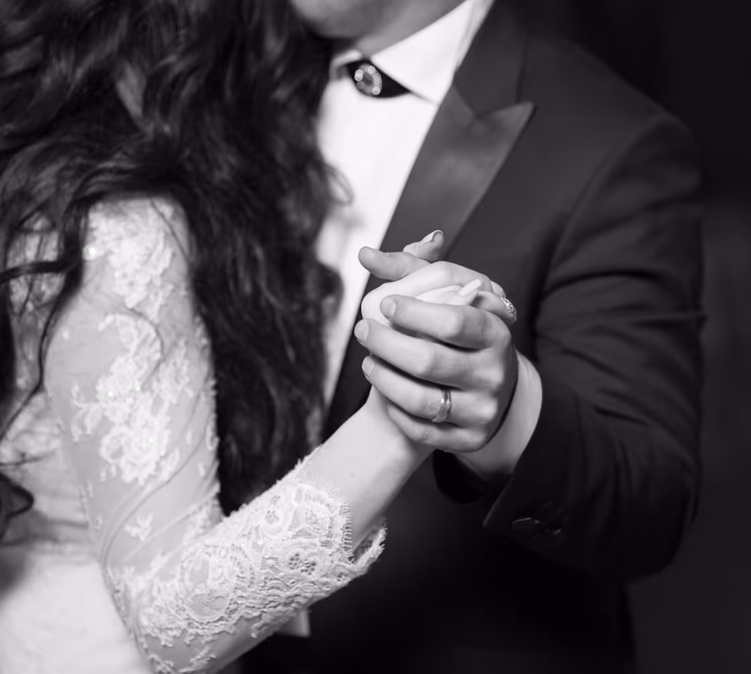 Schwarz-weiß-Foto eines Paares, das sich an den Händen hält und tanzt, die Frau trägt ein Spitzenbrautkleid.