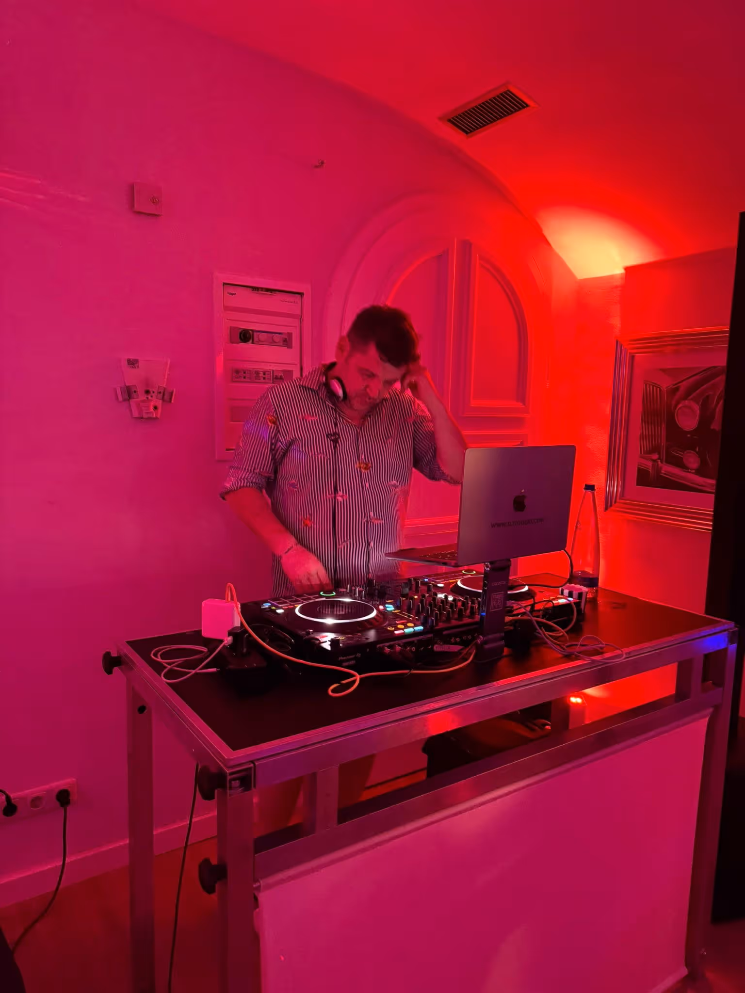 Ein DJ mit Kopfhörern über einem Mischpult am Tisch in einem rot beleuchteten Raum.