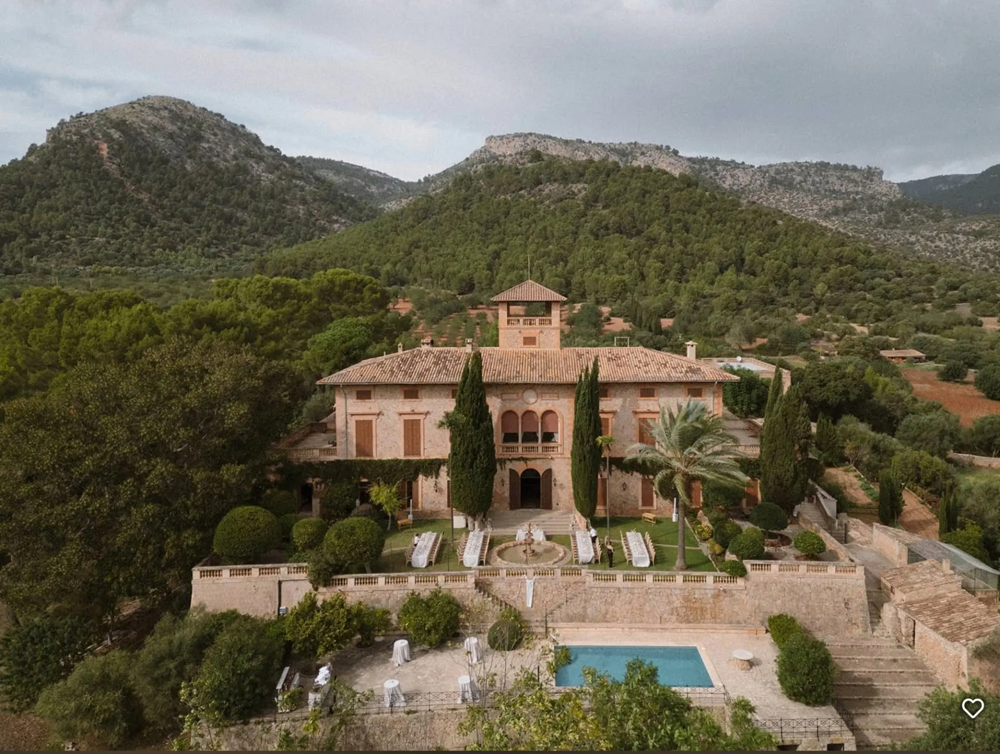 Großes Landhaus mit Terrasse, Brunnen und Swimmingpool, umgeben von Hügeln und üppigem Grün.