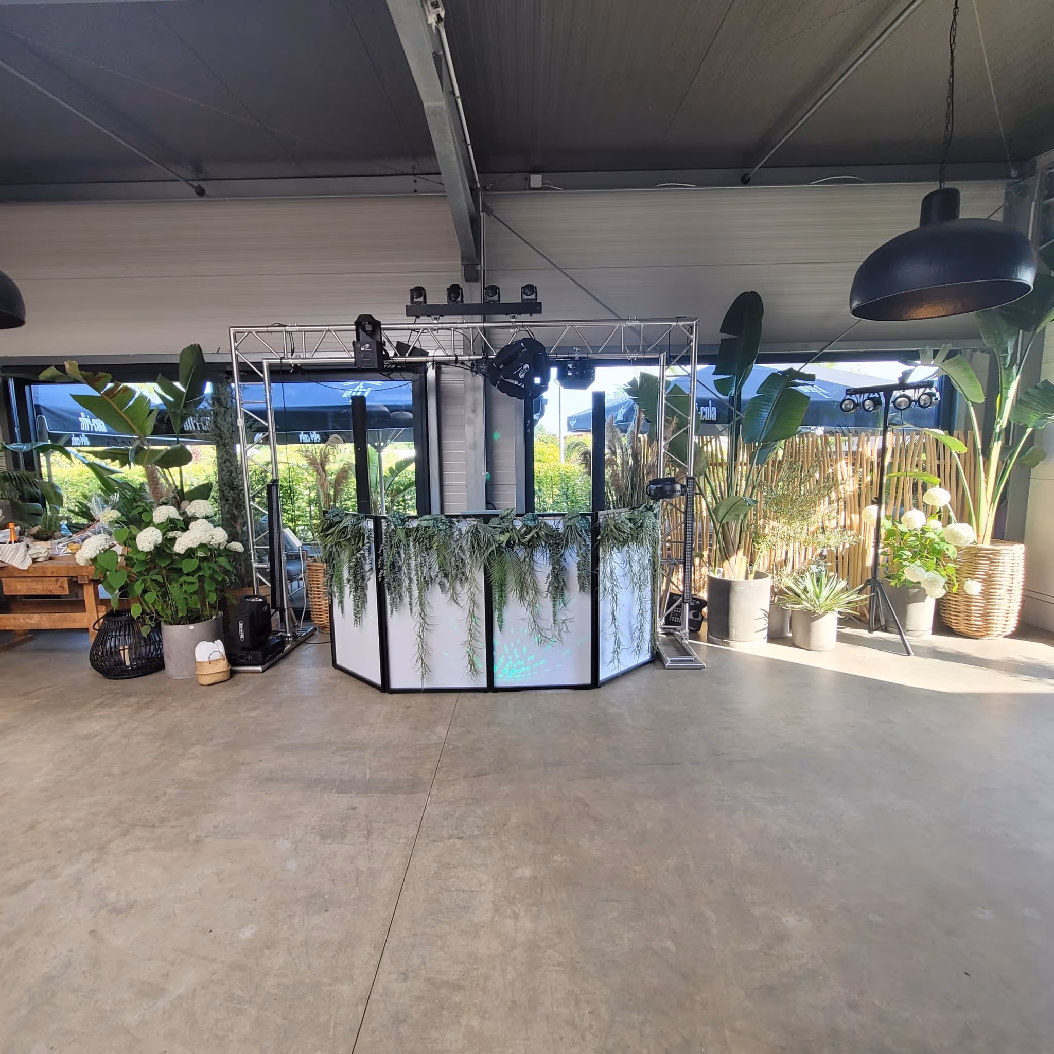 Moderner DJ-Pult mit grünen Pflanzen und großen Lampen in einem hellen Veranstaltungsraum.