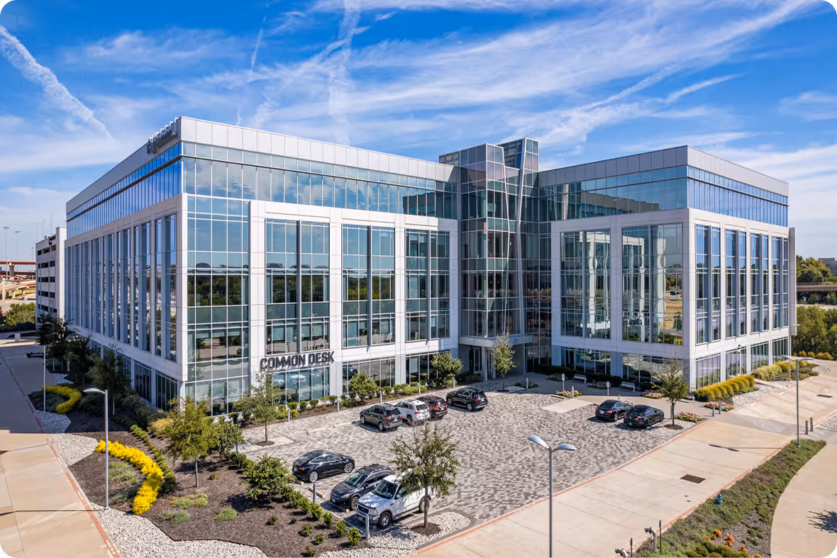 Modern office building with large glass windows and a parking lot with cars under a blue sky.