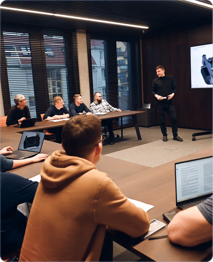 A man presenting to a group seated around a conference table with laptops in a modern meeting room.