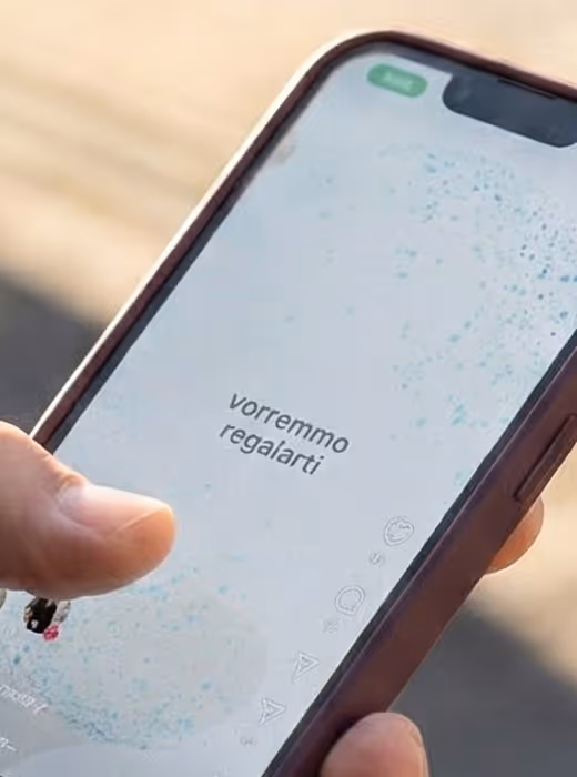 Una mano tiene un telefono cellulare con lo schermo che mostra il testo 'vorremmo regalarti'.