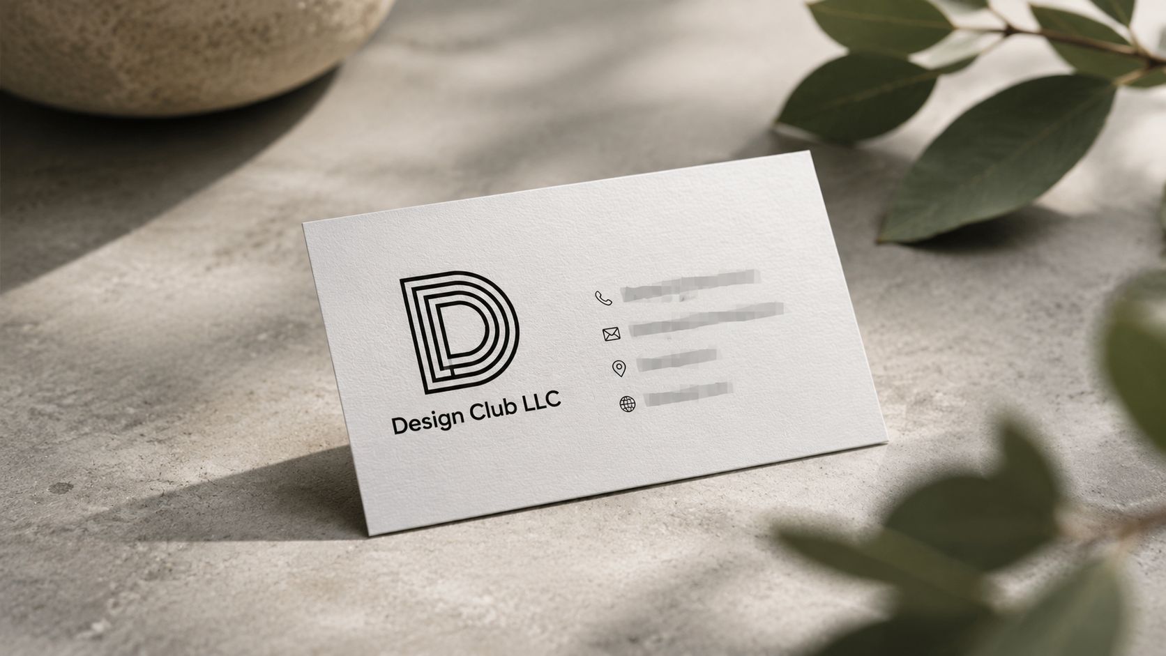 A professional Design Club LLC business card resting on a textured surface with leaves in the foreground.