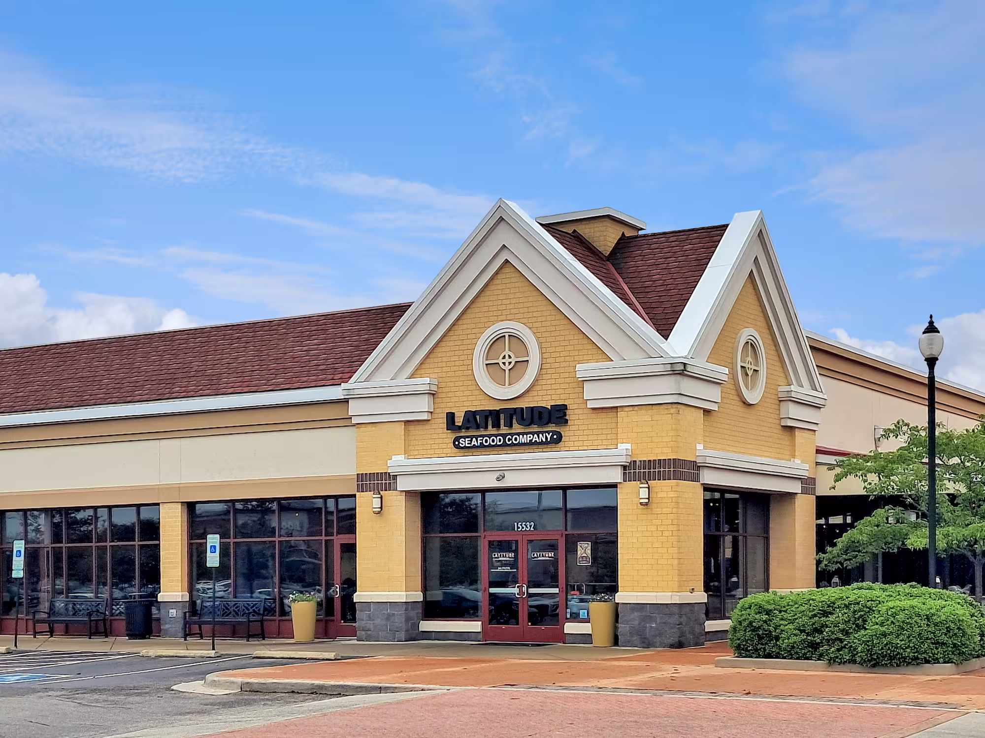 Exterior view of Latitude Seafood Company building with yellow brick facade, red roof, and clear blue sky.