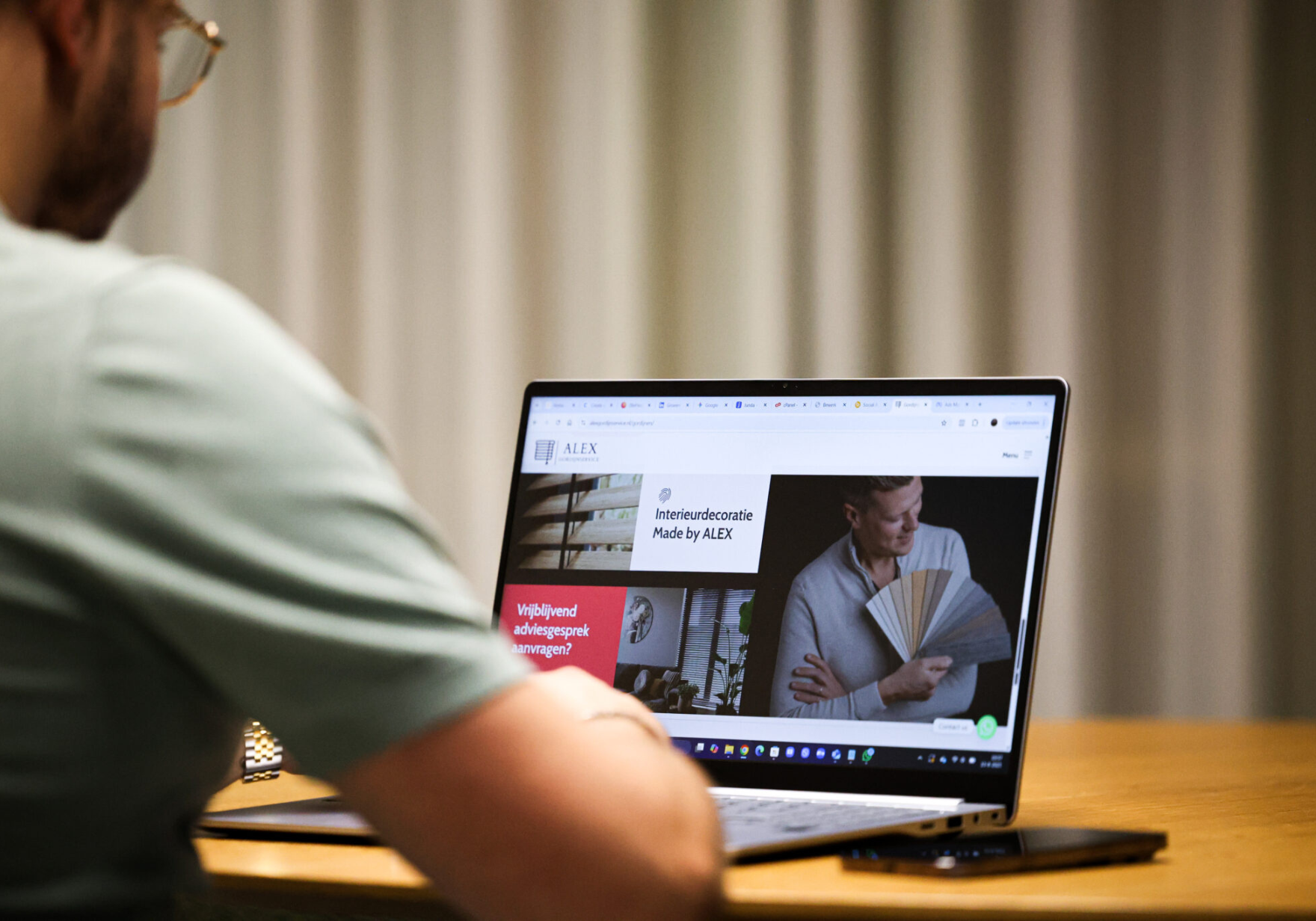 Man die naar een laptop kijkt met een interieurdecoratiesite van ALEX op het scherm.