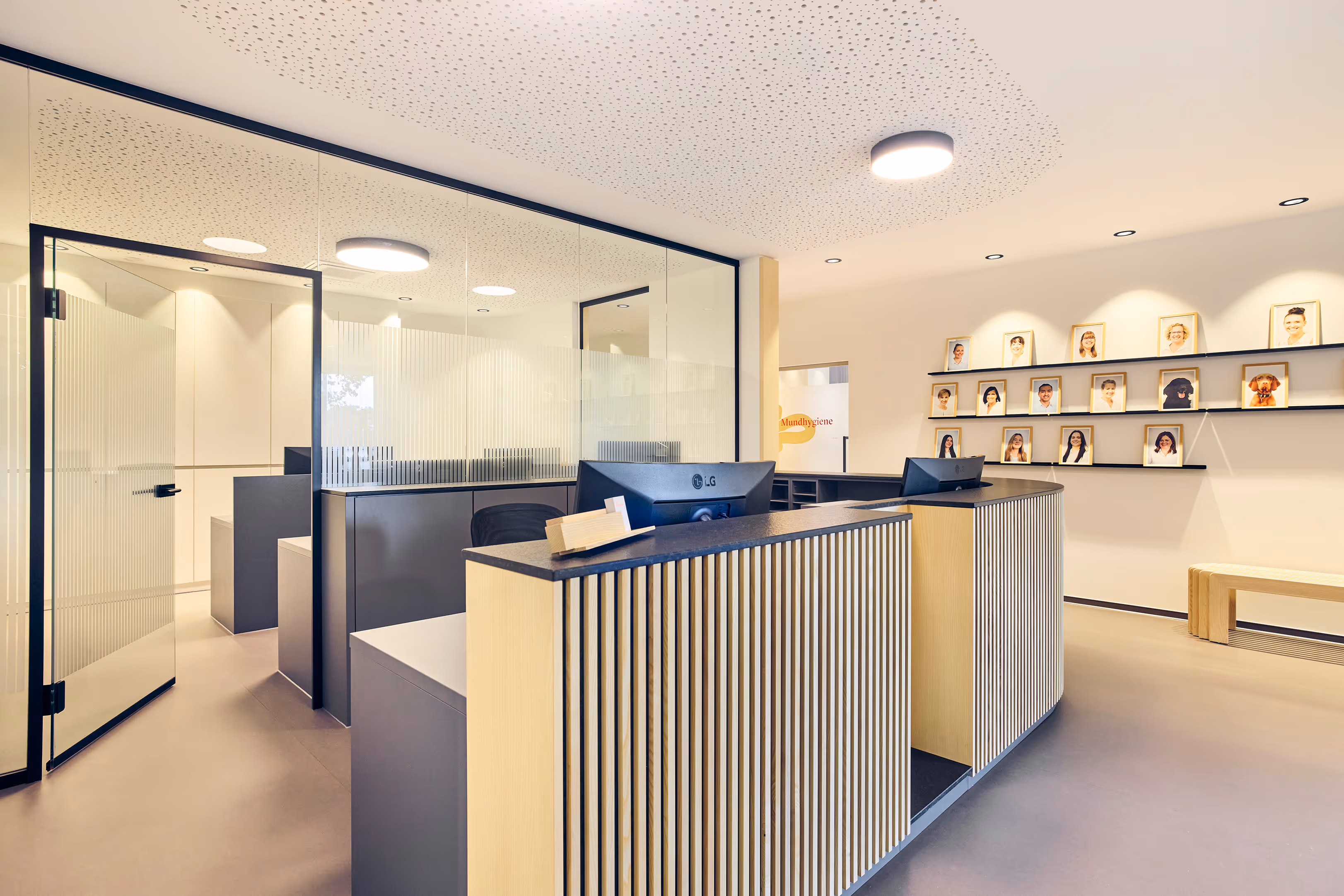Moderner Empfangsbereich mit hölzernem Tresen, Computermonitoren, Glaswand in der Praxis Mundwerk in Moosburg.