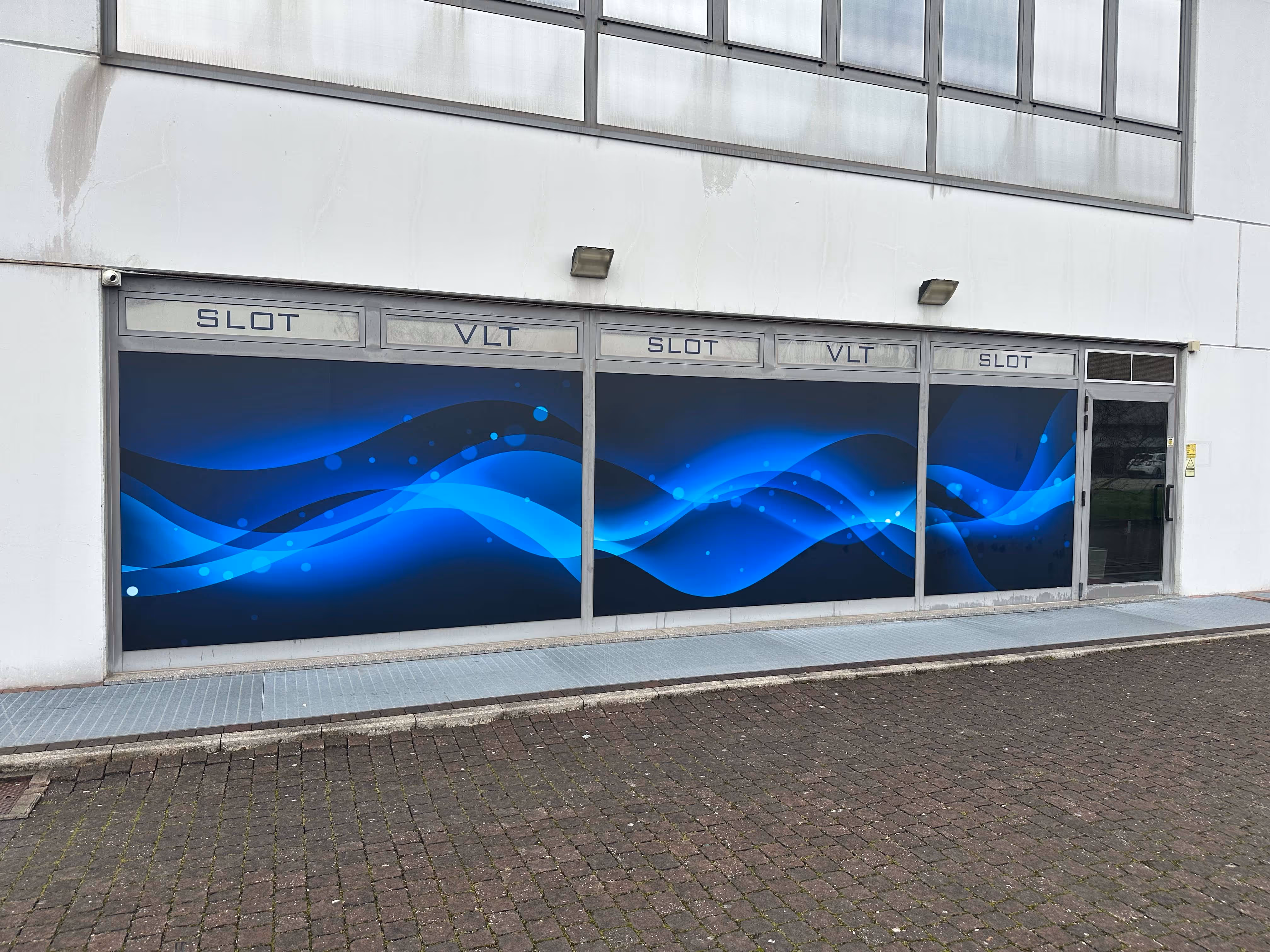Vetrofanie decorative blu per sala slot. Design grafico e schermatura solare per la privacy delle vetrine.