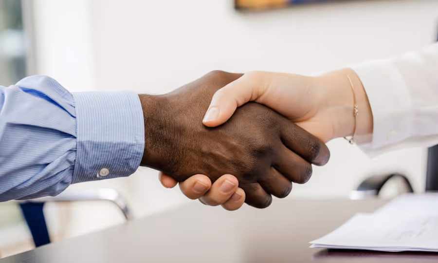 Close-up of a handshake between a person with dark skin wearing a blue shirt and a person with light skin wearing a white shirt, discussing electoral reform.