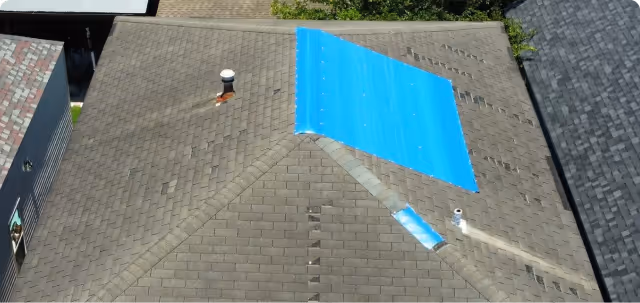 Roof with a large blue tarp covering a damaged section near the ridge.
