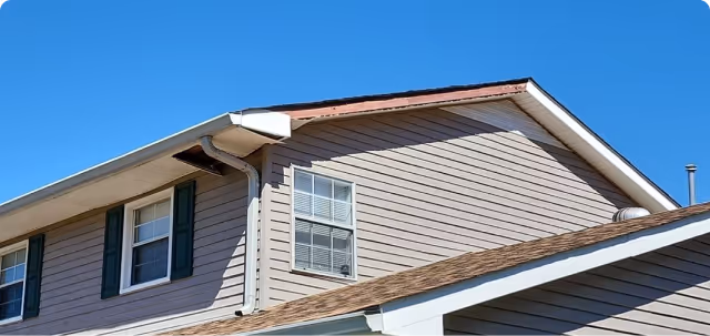 Upper part of a beige house with white trim, green shutters, and clear blue sky background.