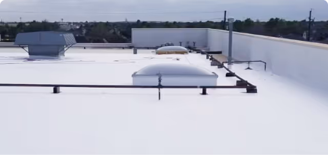 Flat commercial building roof with white membrane, ventilation units, and skylights.