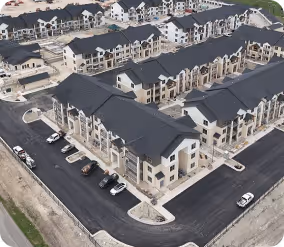 Aerial view of a newly constructed residential apartment complex with multiple buildings and black asphalt roads.