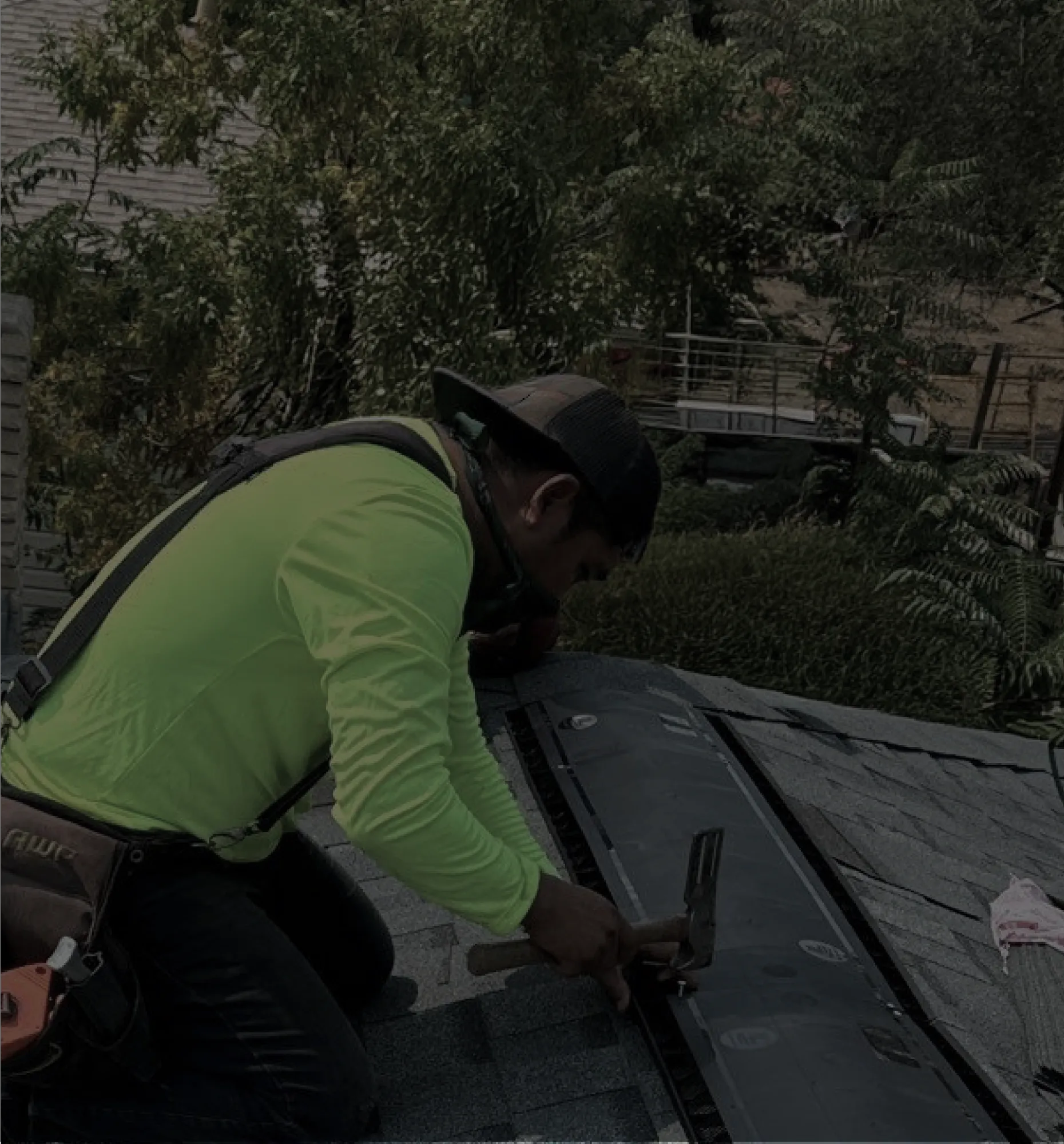 Roofer in a neon green Roofsquad shirt installing asphalt shingles on a roof.