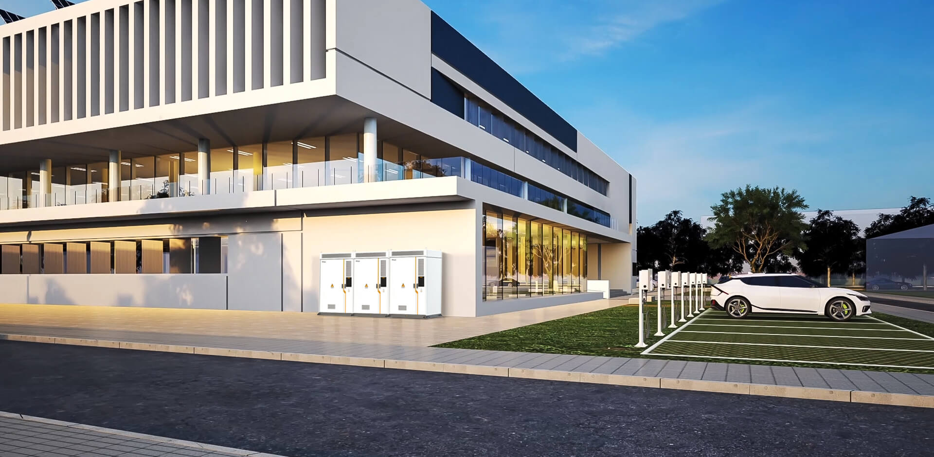 Modernes Bürogebäude mit großen Fenstern und außenliegenden Elektroanschlusskästen neben einem Parkplatz mit einer weißen Elektroauto-Ladestation.