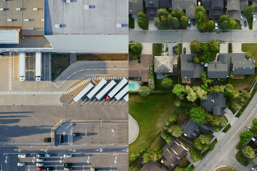 An aerial split view contrasting a commercial warehouse facility with a suburban residential neighborhood.