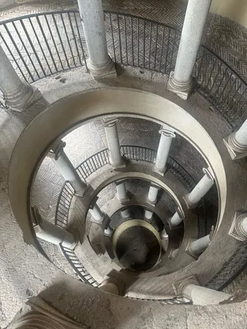 Top-down view of a stone spiral staircase with columns and a black metal railing.