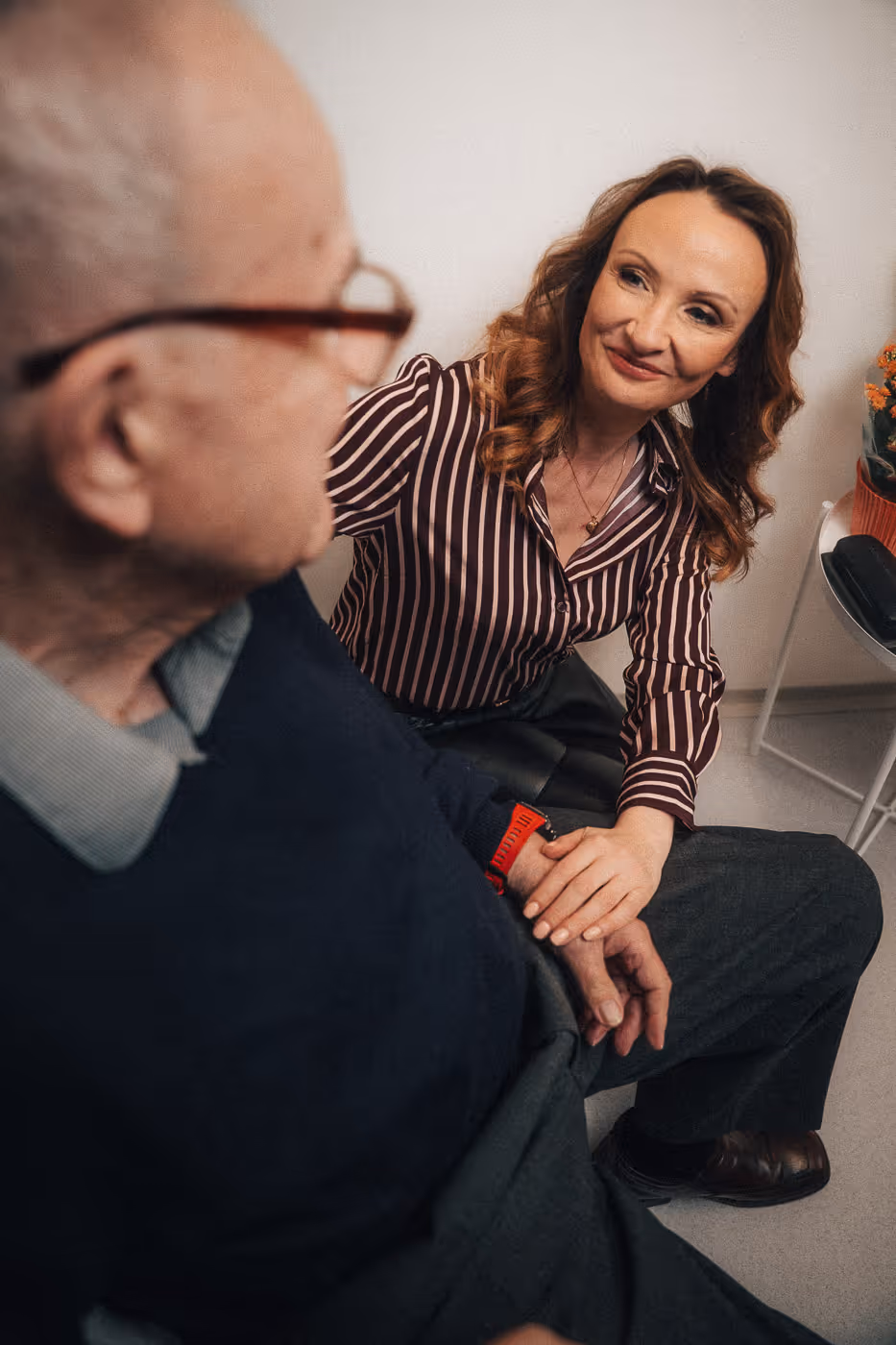 Smiling woman holding hands with an elderly man in a caring gesture during a conversation.